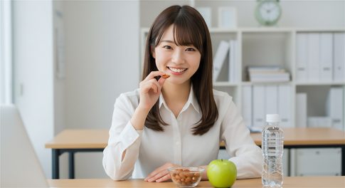 職場のデスクでアーモンドやりんごを楽しむ若い日本人女性。明るいオフィス環境で、健康的なライフスタイルを象徴するシーン。